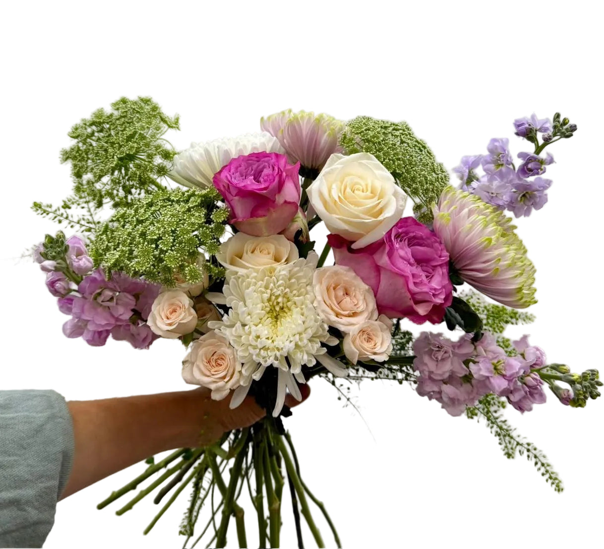 A hand holding a vibrant mixed flower bouquet featuring pink and white roses, cream chrysanthemums, light green filler flowers, and purple delphiniums against a plain light gray background.