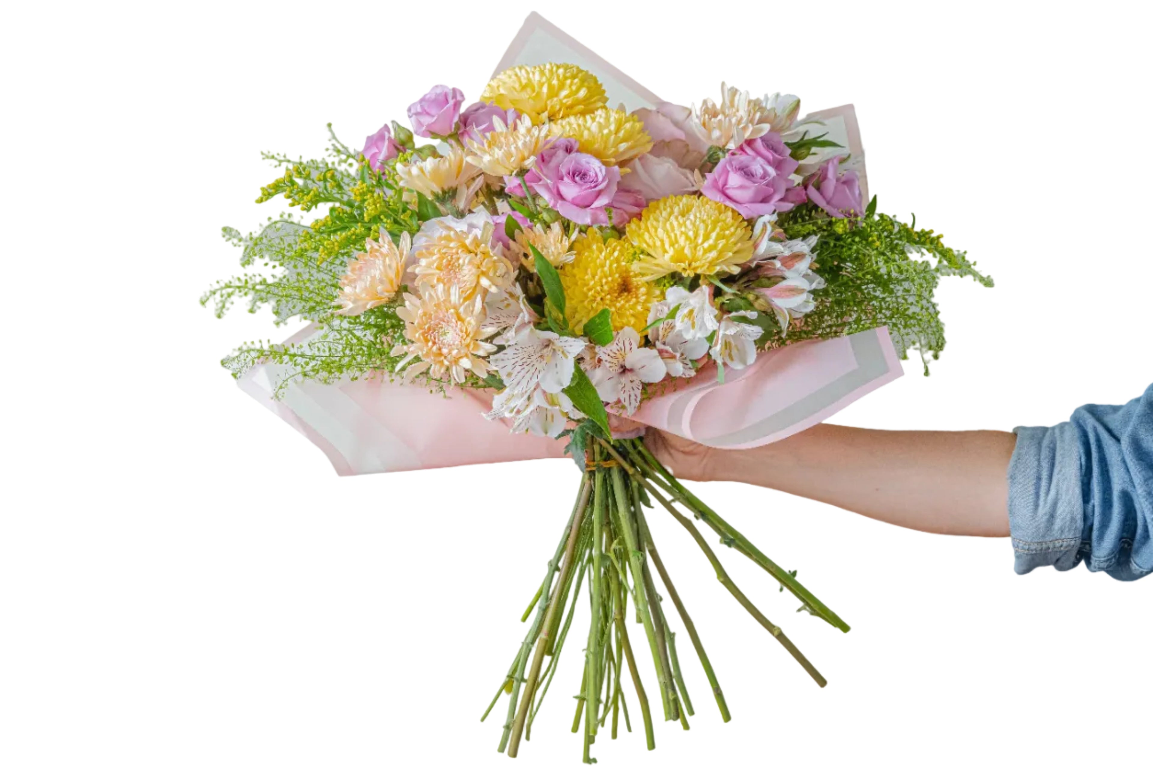 A hand holding a vibrant floral bouquet with yellow chrysanthemums, pink roses, and white alstroemeria wrapped in light pink tissue paper, set against a solid light gray background.